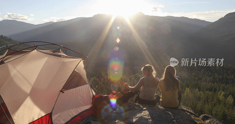 Young women watch the sunset on a mountain ledge campsite
